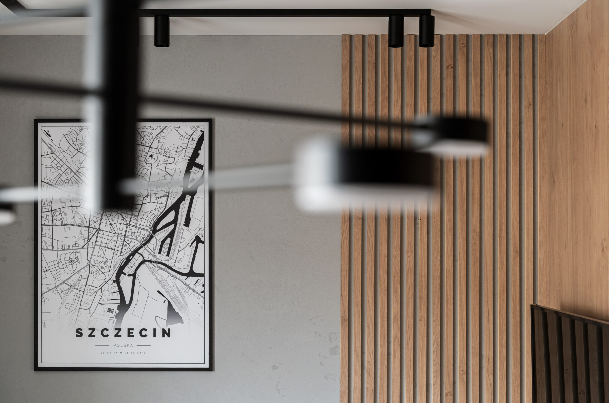 Detal wykończenia salonu: drewniane lamele, szara ściana o strukturze betonu oraz nowoczesny plakat z mapą Szczecina. Staranne prace wykończeniowe i montaż dekoracji zrealizowane przez firmę Remonty Świtaj.